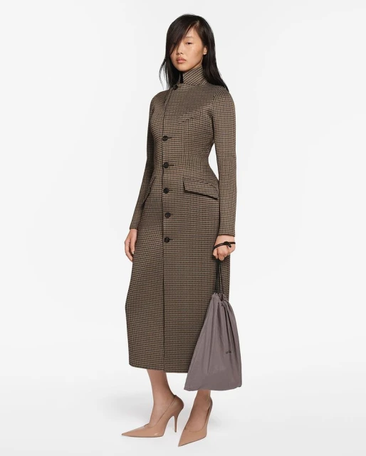 A slender Asian female model showcases a long-sleeved brown and black houndstooth dress, paired with beige heels and a grey drawstring bag.