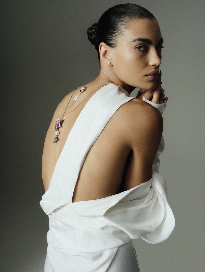 Woman with dark hair in updo wearing white dress and jewelry poses in a photo studio. Light and airy, fashion and beauty style.