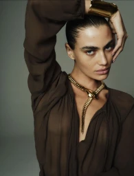 Model in brown blouse with gold snake necklace and cuff bracelet against grey background