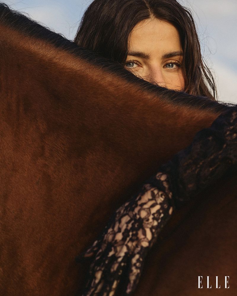 Model embracing a horse outdoors with a dark lace sleeve. The composition is a close-up of the model's face next to the horse.