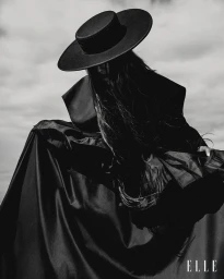 Model Isabeli Fontana wearing a wide-brimmed flat hat and dark structured coat against an overcast sky for Elle Brasil.