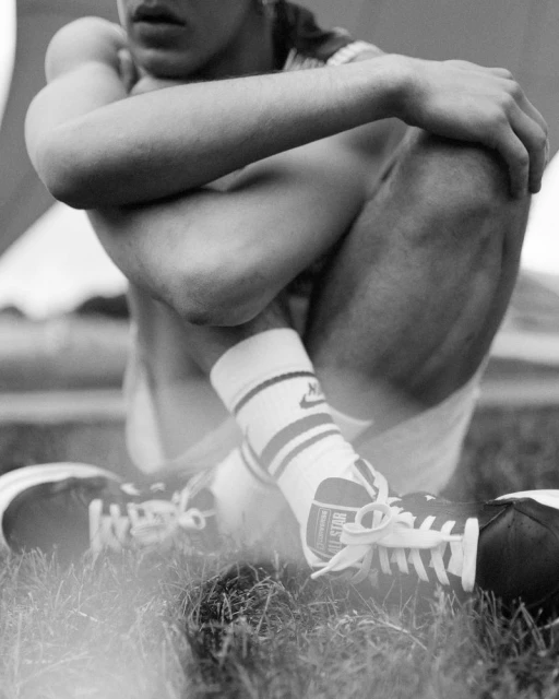 Monochromatic shot of a man sitting on grass with shoes and socks on, posing with arms on knees, black and white photography.