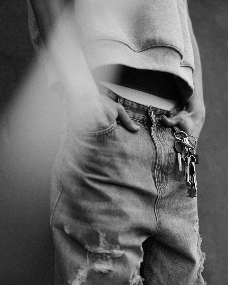 Close-up black and white shot of an adult wearing jeans and a cropped sweatshirt with keys hanging from the jeans.