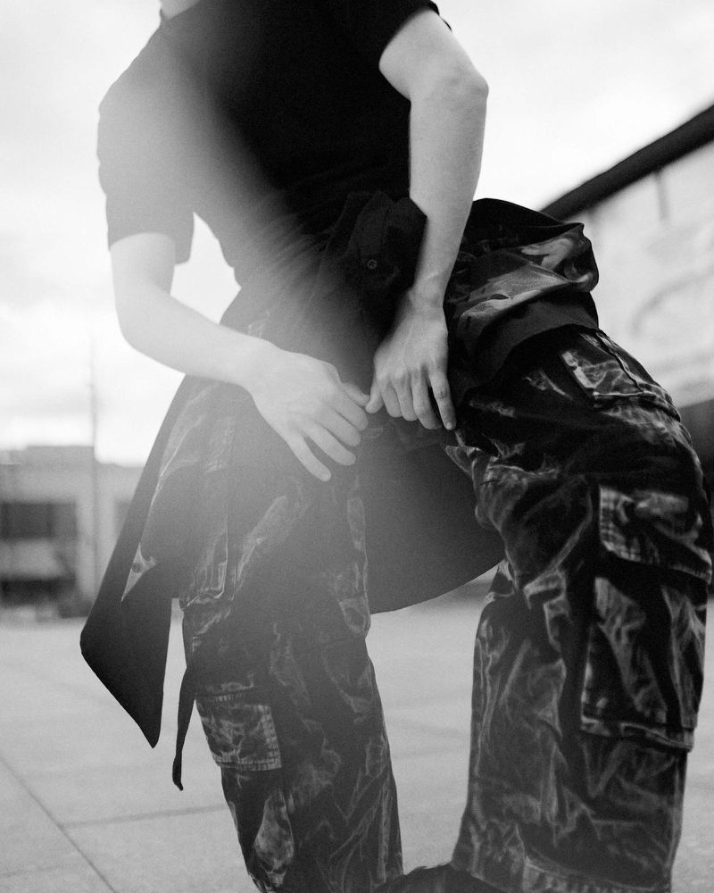Monochrome low-angle portrait of a person wearing cargo pants and a dark t-shirt with strong light flare in an outdoor setting