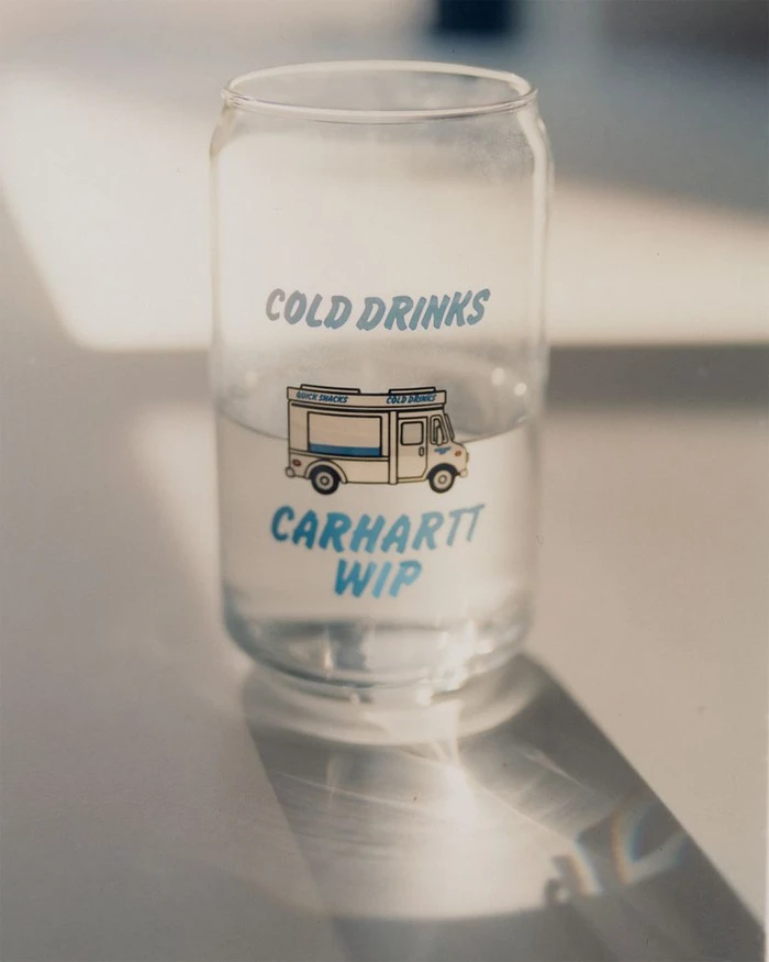 Clear glass can filled with water featuring blue printed text and a graphic of a van, resting on a white surface.