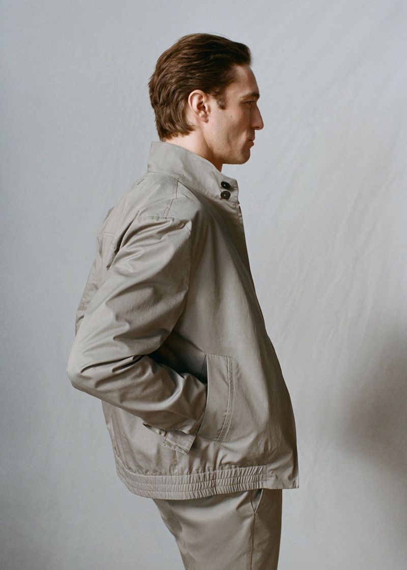Profile shot of an adult male in a light brown jacket and pants against a plain backdrop in a studio setting, fashion oriented.
