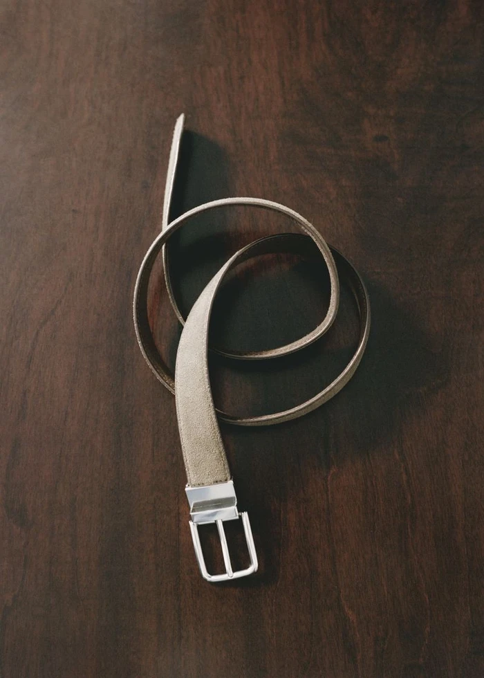 Coiled leather belt with a silver buckle resting on a dark wood surface