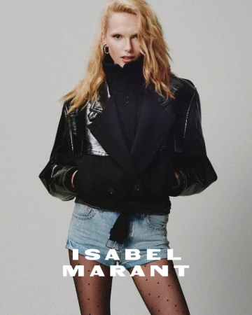 Model with blonde hair wearing a black jacket and denim shorts against a neutral grey background