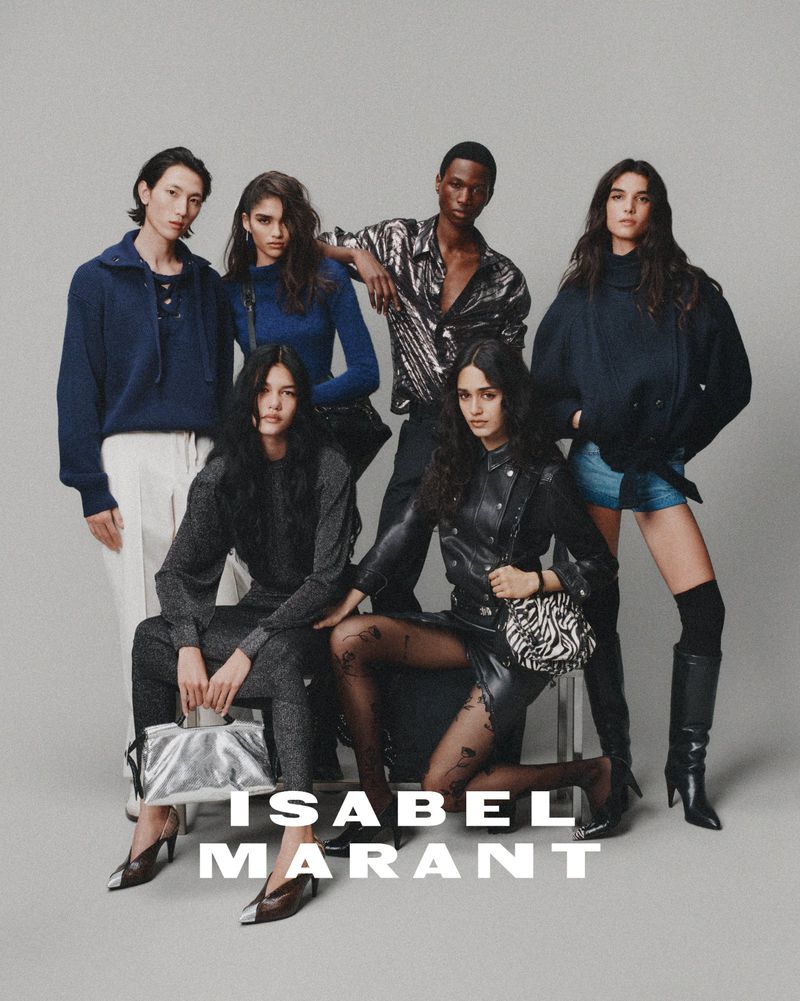 Group of fashion models showcasing a new collection, posing in studio with a neutral backdrop. Dark and blue tones dominate the apparel.