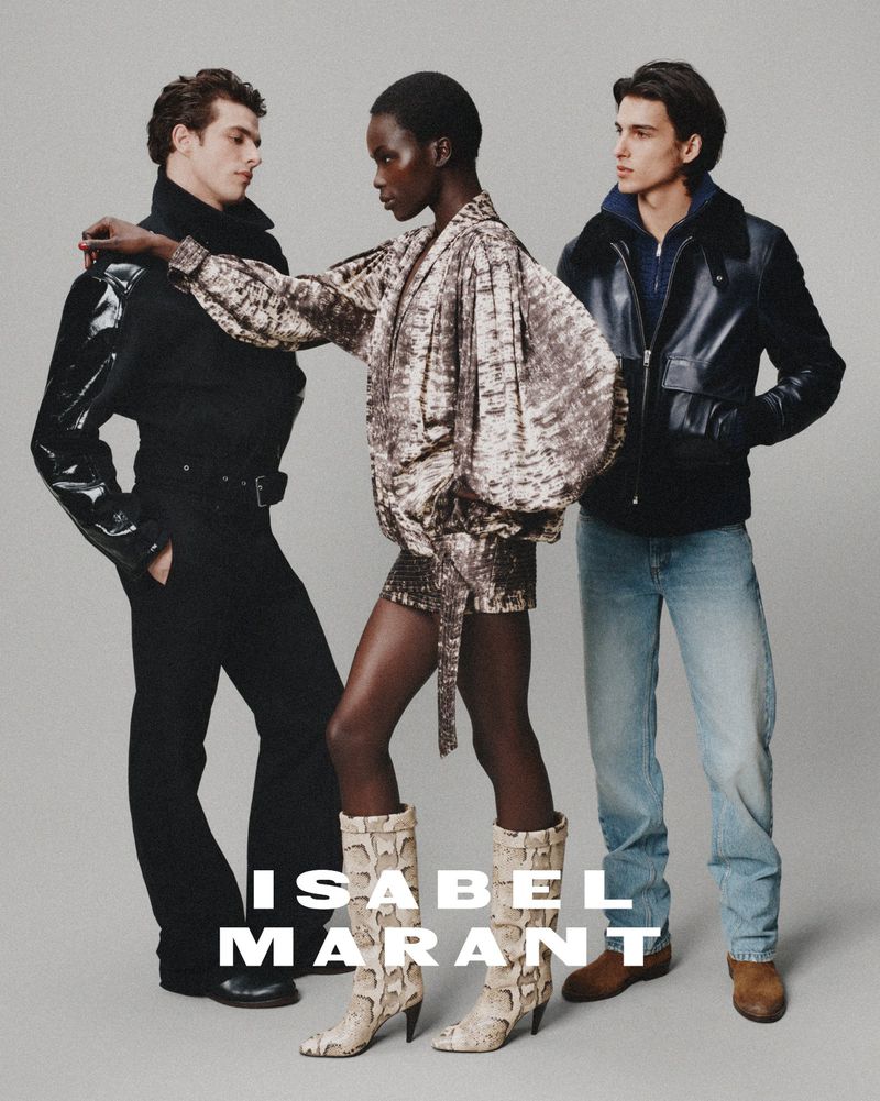 Isabel Marant fashion ad featuring three models in an indoor studio setting, wearing stylish jackets, tops, pants, and distinctive snake print boots.