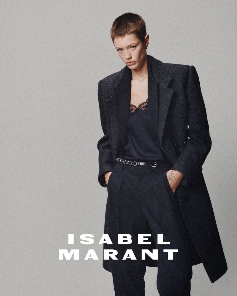 Model with short buzzcut wearing a dark wool coat and trousers against a neutral grey seamless background