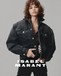 Model with curly brown hair wearing a dark denim jacket against a neutral grey studio background for Isabel Marant.