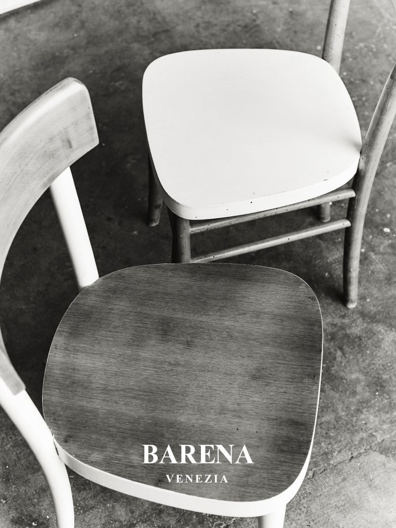 High-angle shot of two minimalist wooden chairs in a black and white photograph, featuring the brand name BARENA VENEZIA.