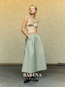 Model wearing a matching beige bralette and sage green midi skirt with a chunky beaded necklace against a textured backdrop
