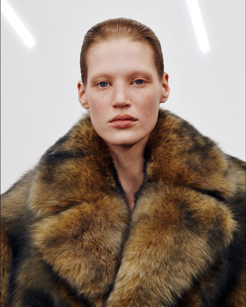 Close-up studio portrait of a fair-skinned adult female wearing a brown and black fur coat, posing against a white backdrop.