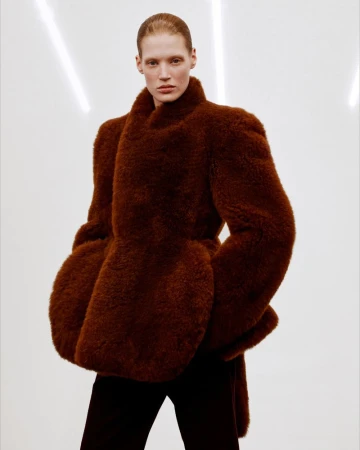 Model wearing a structured brown textured coat against a bright white seamless background with vertical light streaks.