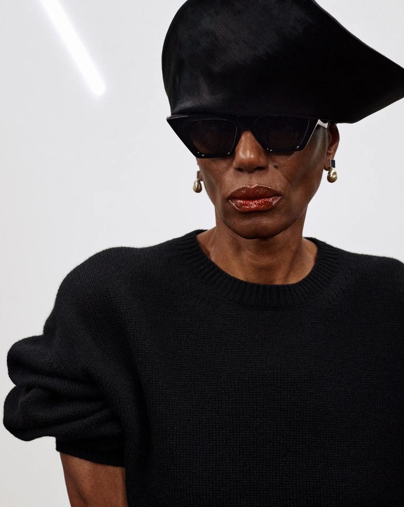 Stylish woman in black sweater and hat with sunglasses. Studio shot on a white background with modern fashion aesthetic.