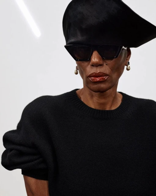 Stylish woman in black sweater and hat with sunglasses. Studio shot on a white background with modern fashion aesthetic.