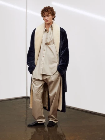 Fashionable adult man wearing oversized beige shirt and pants with a large navy blue faux fur coat with a cream colored lining.