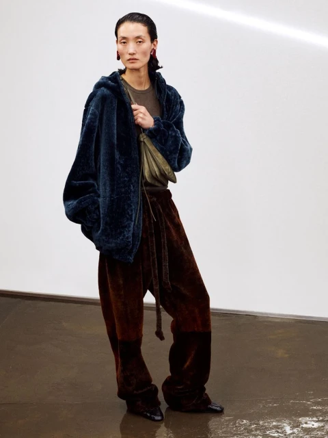 A person poses in a photo studio wearing a navy blue jacket, brown pants with a tie at the waist, and black shoes.