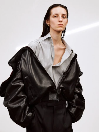 Model wearing a black leather jacket and striped shirt against a plain white studio backdrop.
