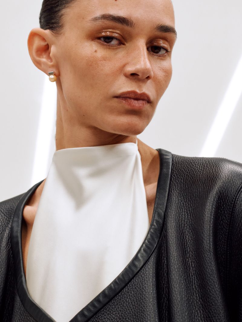 Headshot of a light-skinned adult female wearing a black leather jacket with a white shirt against a brightly lit white background.