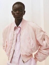 Model wearing a light pink bomber jacket and button-down shirt against a seamless white studio background.