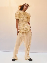 Model in textured cream top and loose trousers posing against a plain wall shot by Alasdair McLellan for Phoebe Philo.