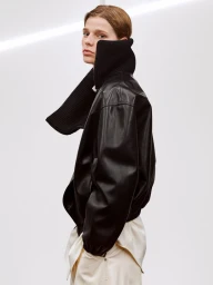 Model in black leather jacket with high ribbed collar against a plain white studio background
