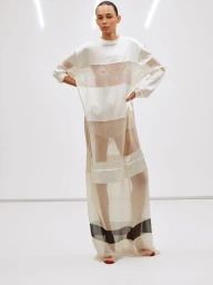 Model wearing a sheer white striped top and long skirt standing against a white studio wall