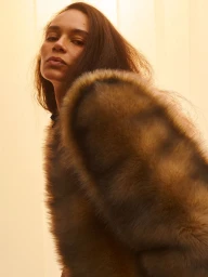 Portrait of a model wearing a textured brown faux fur coat against a warm neutral background, photographed by Alasdair McLellan.