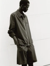 Model Mamuor Majeng wearing a dark zipped shirt and matching shorts against a white background for Drykorn SS26.