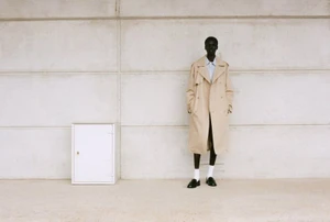 Model Mamuor Majeng in a beige trench coat standing against a pale tiled wall for Drykorn SS26.