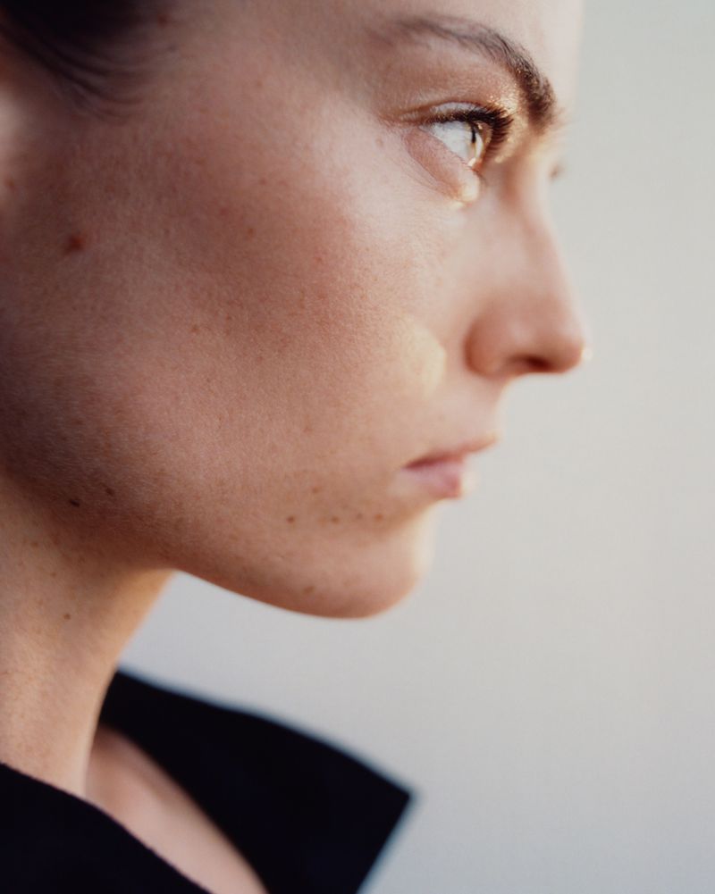 Close-up profile portrait of a woman with freckles and dark clothing against a neutral background