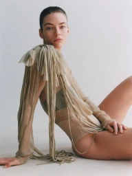 Model seated wearing a sheer fringe top against a neutral studio background for The Gentlewoman.