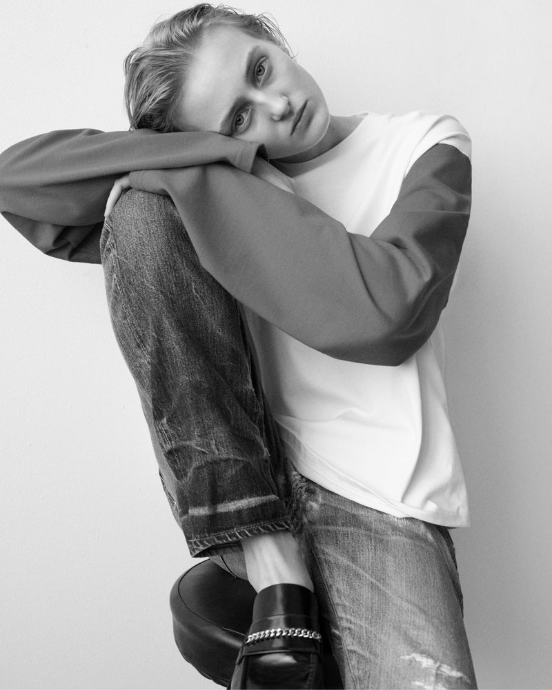 Monochromatic portrait of a slender female model posing indoors with blue jeans, black loafers and a two-tone, long-sleeved t-shirt.