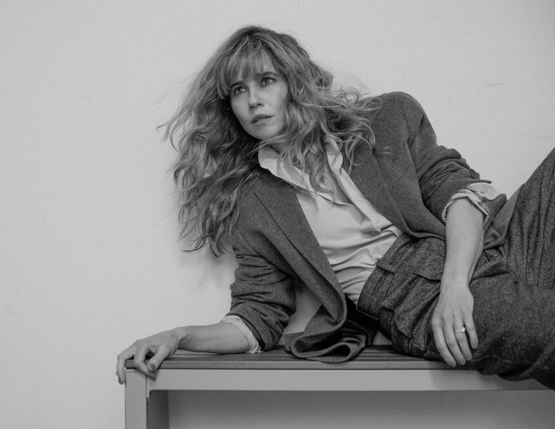 Black and white portrait of Linda Cardellini reclining on a bench wearing a tailored blazer and trousers for Numero Netherlands.