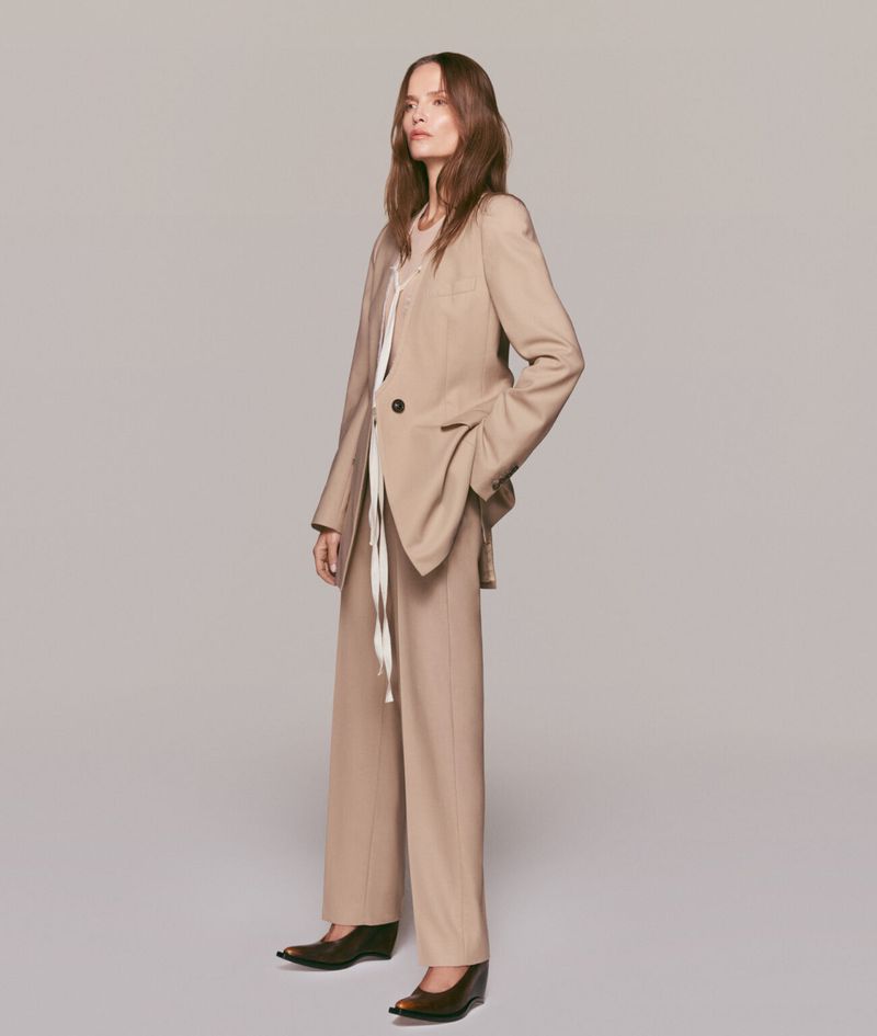 Fashionable woman in a tan blazer and pants poses in a studio. The neutral color palette enhances the professional, yet casual style.