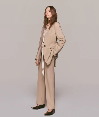 Fashionable woman in a tan blazer and pants poses in a studio. The neutral color palette enhances the professional, yet casual style.