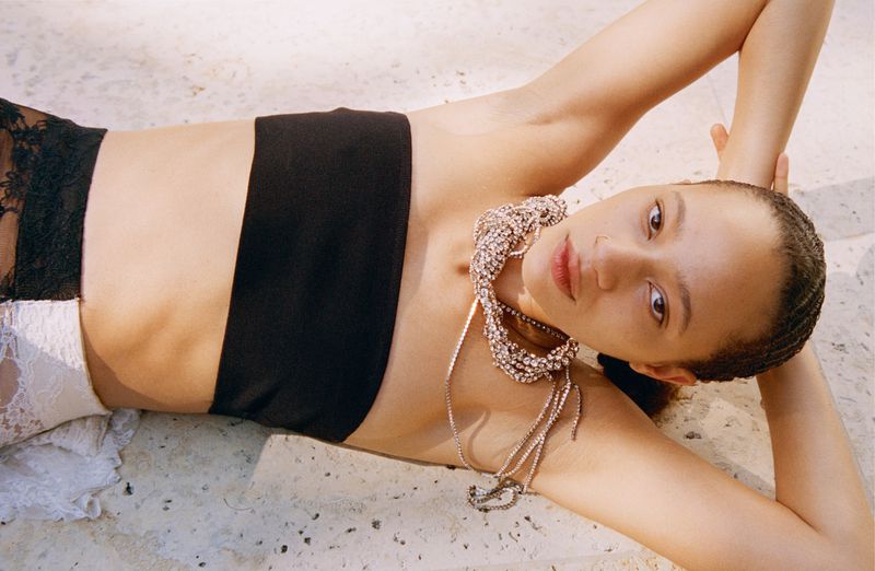 Woman with dark hair and a black top lies on a stone surface while wearing a silver crystal necklace in an outdoor setting with natural light.