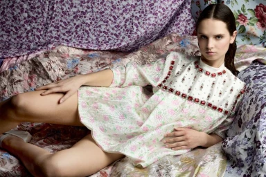Model Giselle Norman reclining on patterned floral fabrics wearing a jeweled white dress for 10 Magazine Japan.