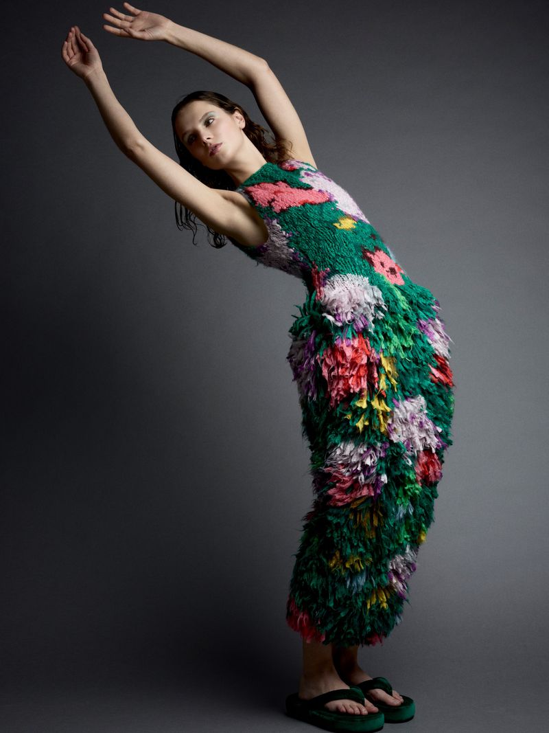 Elegant woman in a floral textured dress strikes a pose in a studio. The dress has an organic texture, and the backdrop is grey.
