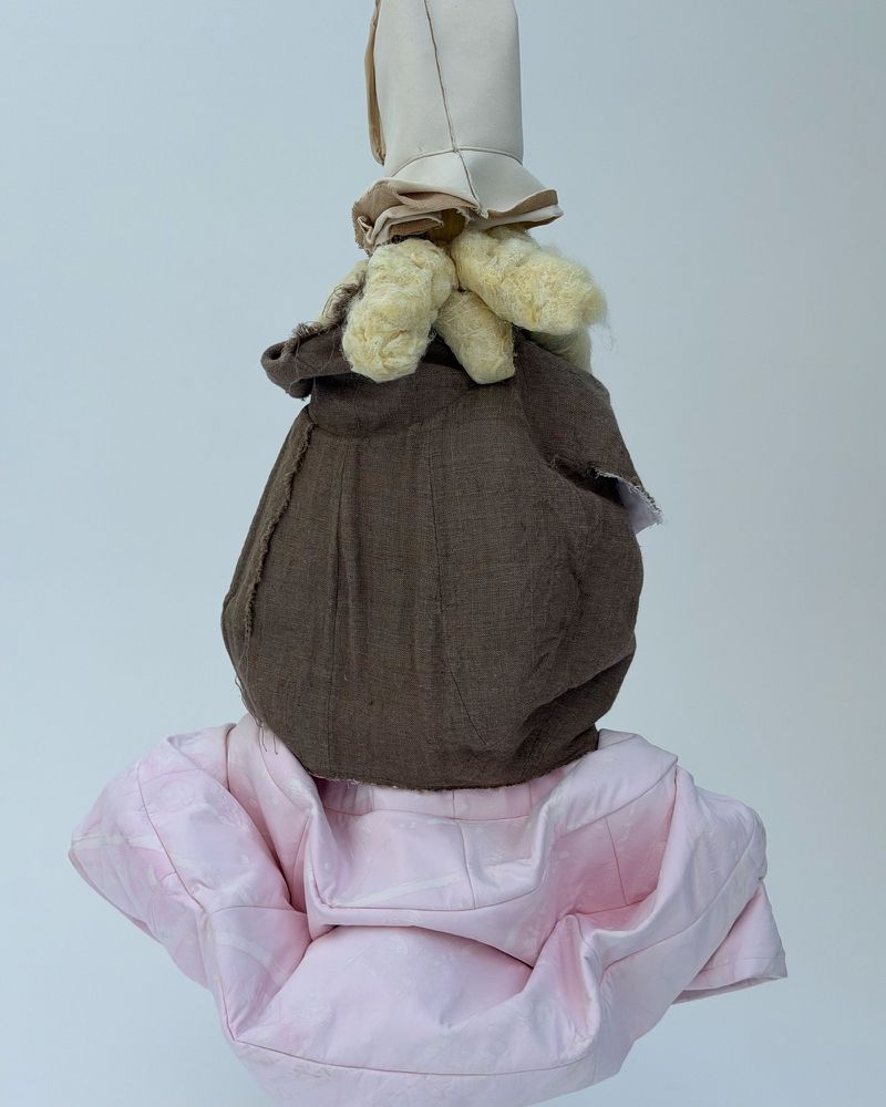A still life shot in a photo studio featuring a stack of doll clothes in pink, brown and tan fabric, creating a surreal, soft sculpture.