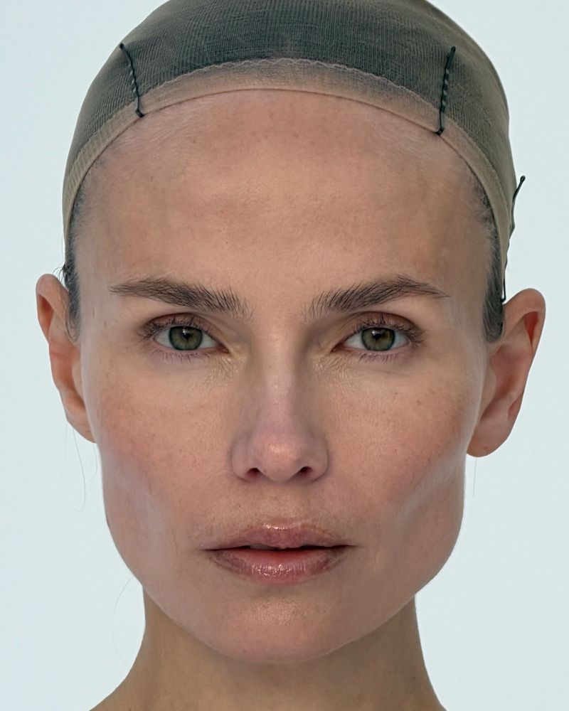 Close-up portrait of a fair-skinned woman with green eyes wearing a hair cap, against a bright white background, focusing on facial features.