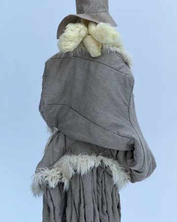 Unique grey woven garment with light-colored fringed accents and matching hat, set against a bright white backdrop in a studio shot.