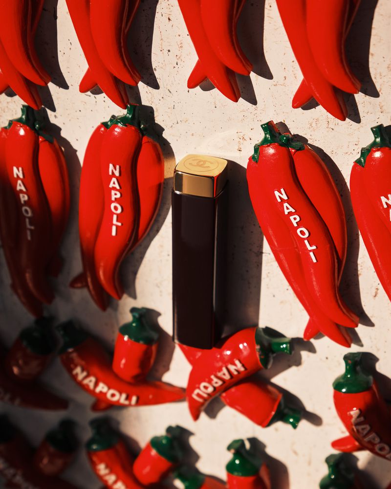 Chanel lipstick tube stands out among vibrant red chili pepper magnets, adding a touch of beauty to a kitchen decor display.