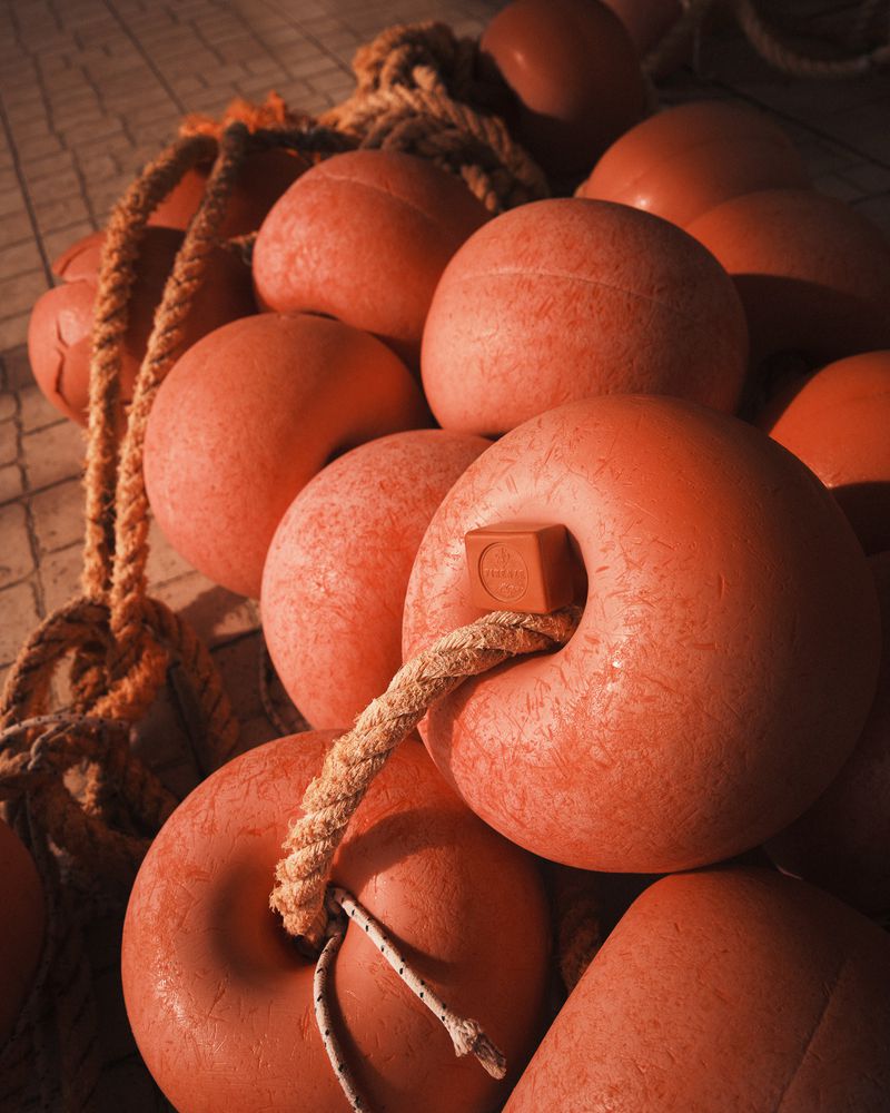 Close-up of vibrant orange fishing net floats with thick ropes, arranged on a textured surface in warm, diffused lighting, creating depth.