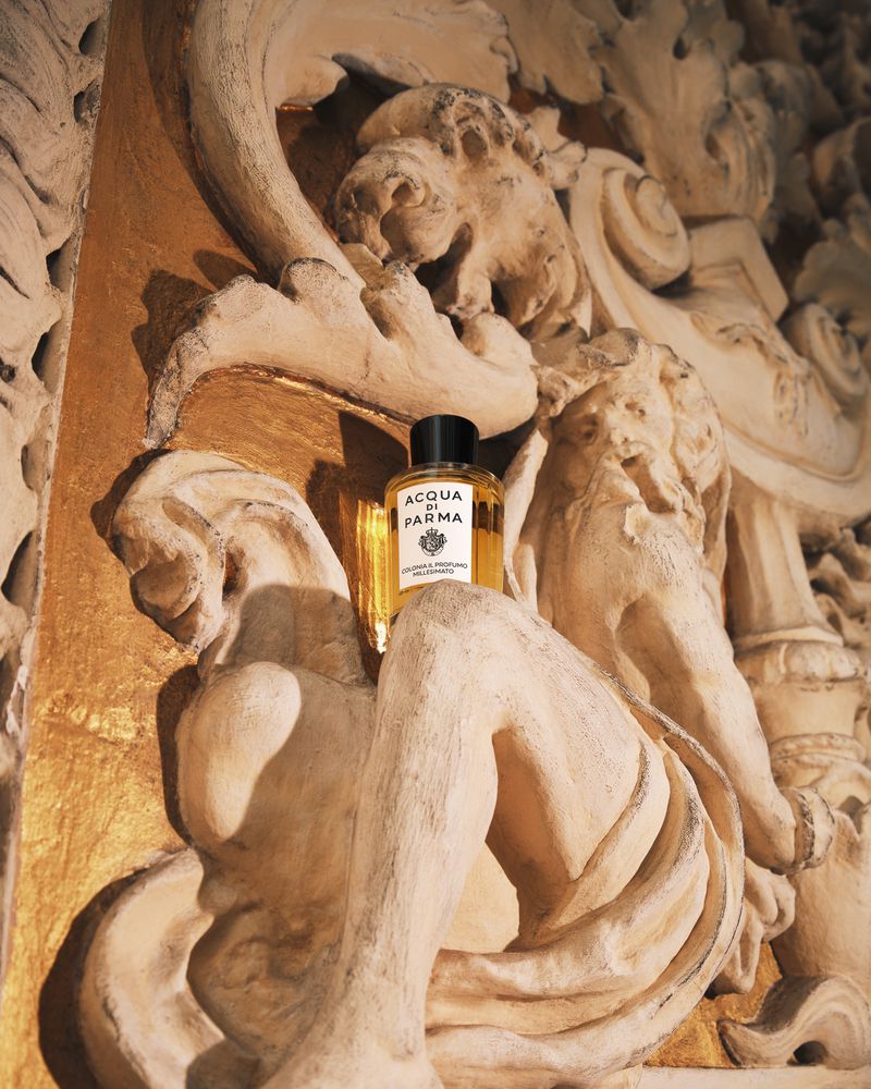 Acqua di Parma cologne bottle sits on a tan, carved stone surface in a close-up shot, highlighting its packaging and luxurious presentation.