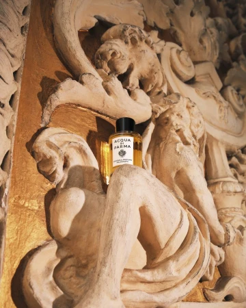 Acqua di Parma cologne bottle sits on a tan, carved stone surface in a close-up shot, highlighting its packaging and luxurious presentation.