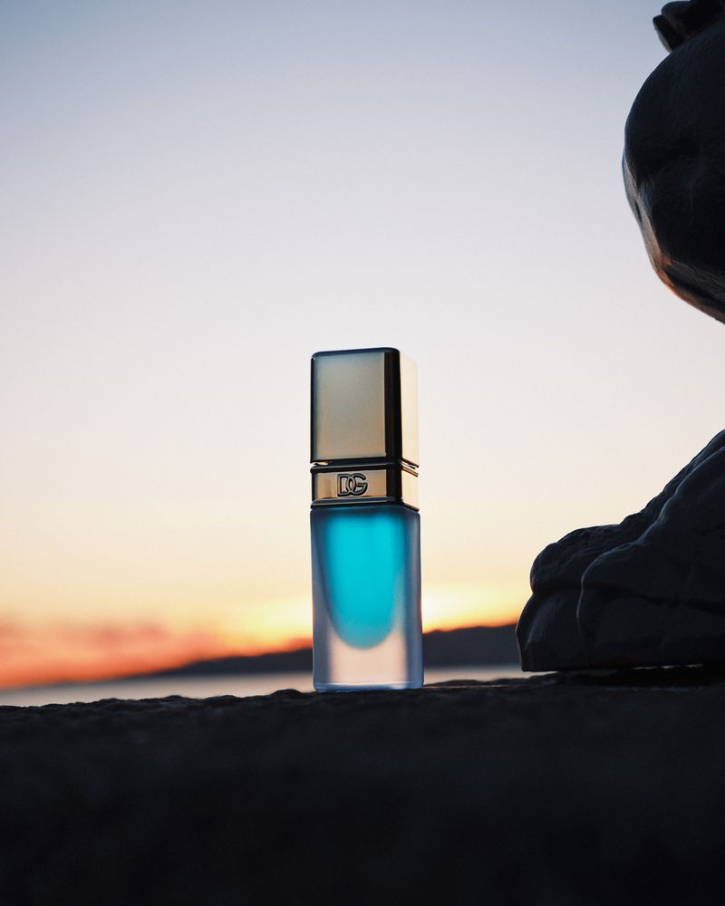 Dolce & Gabbana perfume bottle on a rock with a sunset backdrop, reflecting luxury and sophistication in a natural setting.